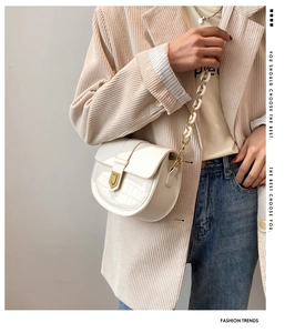 Detail of white saddle bag with crocodile texture and decorative resin chain strap
