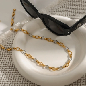 Detail of two-tone gold and silver link chain necklace in a white tray with sunglasses
