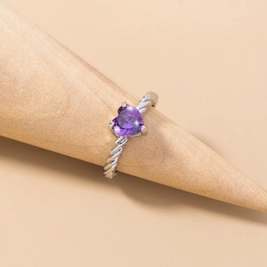 Detail of a silver twisted band ring with a heart-shaped purple gemstone on a wooden stand