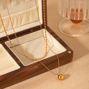 Double layered gold stainless steel necklace with round bead pendant on wooden box