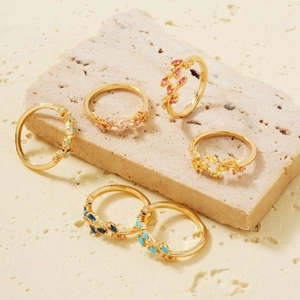 Detailed view of five gold leaf rings with colorful gemstones on a beige stone