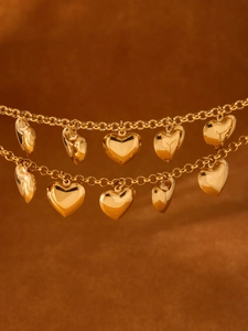 Detail von 18k vergoldetem doppellagigem Kettenarmband mit polierten Herzanhängern