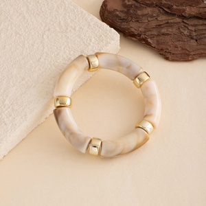 Detail of beige marble resin tube bracelet with gold spacers on natural stone background