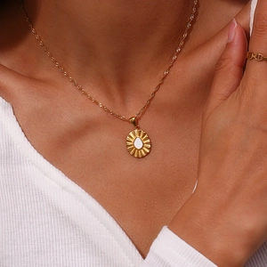 Close-up of gold oval sunburst pendant necklace with white water-drop element on model