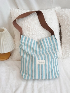 Minimalist blue striped canvas tote bag with brown straps on a white bedding background