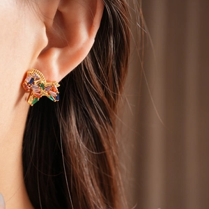 Close-up of gold stud earring featuring colorful zircon stones on model with blurred background