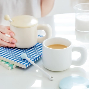 Minimalist white ceramic mug set with colorful lids and spherical spoons on a cozy table