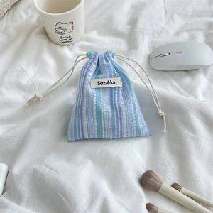 Close-up of pleated striped drawstring storage pouch with Sozakka label on soft bedding