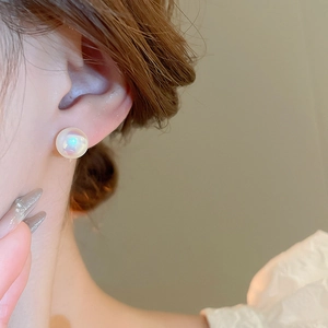Close-up of iridescent mermaid pearl stud earring with gold plating worn by a model