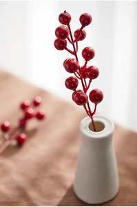 Close-up of bright red artificial Christmas berry stems in a minimalist white vase