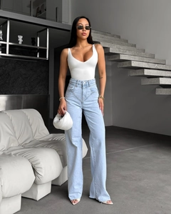 Jean évasé taille haute bleu clair classique porté avec un body blanc et un sac à main