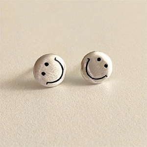 Detail of brushed 925 sterling silver stud earrings with minimalist black smiley face