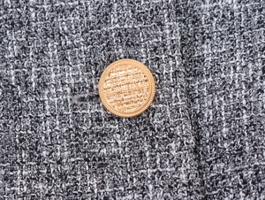 Close-up of black and white tweed fabric with detailed golden textured button