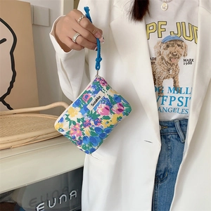 Floral makeup pouch with blue rope handle and brand label held in a hand