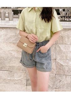 Detail of khaki textured crossbody bag with gold lock worn by a model in casual outfit
