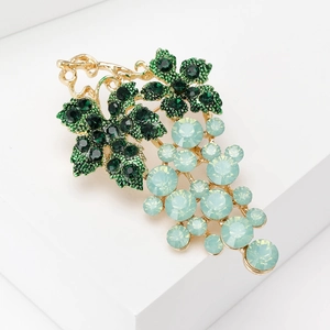 Detail of elegant grape brooch with light blue crystal stones and green leaf design