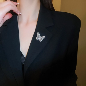 Detailed view of a silver butterfly brooch with teardrop zircons on a black blazer lapel