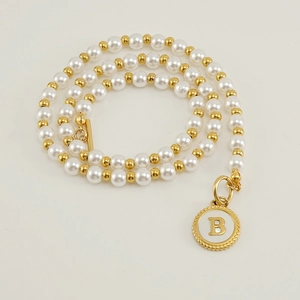 Detailed macro view of gold plated pearl necklace with a white enamel letter B pendant
