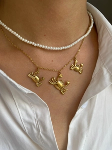 Detail showing gold crab pendants and layered white pearl necklace on collarbone