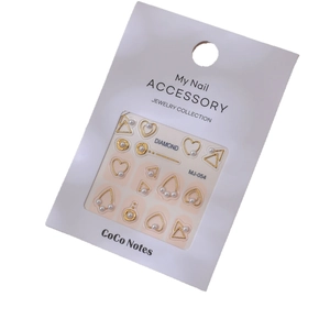 Golden geometric nail art charms with pearls and heart shapes on a white card display
