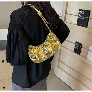 Glossy gold pleated cloud bag shown on model in a minimalist urban lifestyle setting