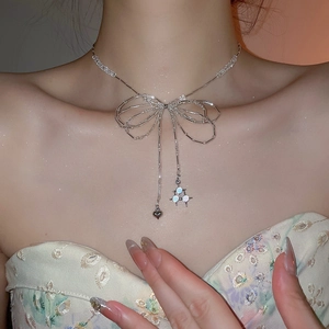 Detail of silver bow necklace with beaded chain heart and planet charms on neck