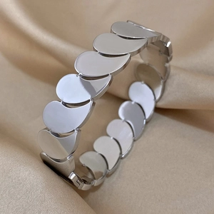 Détail du bracelet argenté multicouche au design goutte sur un tissu en soie champagne