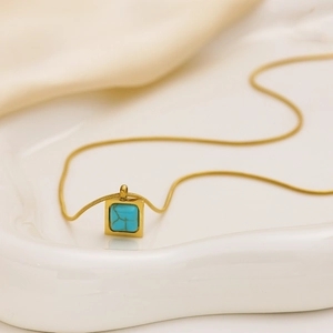 Détail d'un pendentif turquoise carré sur une chaîne en titane doré sur tissu en soie