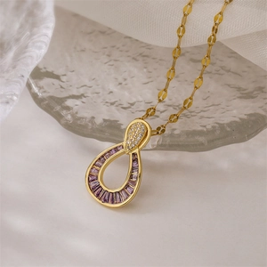 Detail of a gold teardrop necklace with purple baguette gems on a frosted glass edge