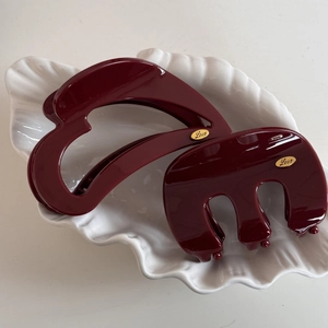 Detailed view of wine red shark hair clips with golden Love emblem on a ceramic plate