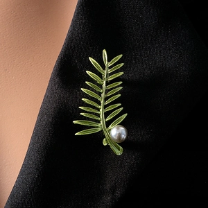 Detailed view of a green leaf brooch with a pearl on a black suit lapel