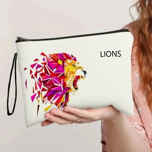 White canvas lion print cosmetic bag with geometric design and wrist strap held by hand