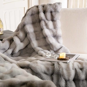 Close-up of thick faux rabbit fur blanket with soft grey gradient texture on a sofa