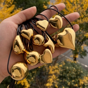 Handheld display of multiple gold heart, star and water drop pendants on black wax cords