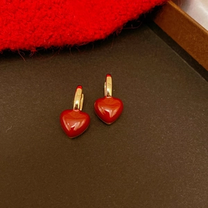 Detailed view of red heart drop earrings with gold hoops on dark textured background