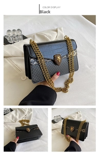 Detail of black crocodile texture bag featuring gold lion head buckle and chunky chain strap