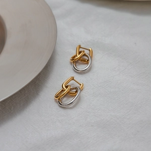 Détail des boucles d'oreilles créoles bicolores entrelacées or et argent sur lin blanc
