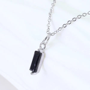 Macro shot of silver chain with rectangular black gemstone pendant on white background