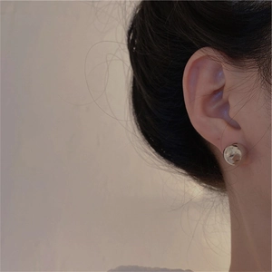 Polished metallic ball stud earrings with hammered texture on a model's ear