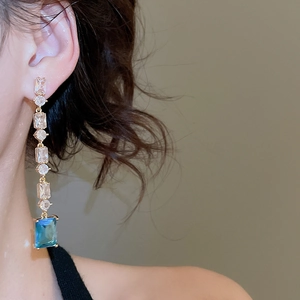 Close-up of 18K gold plated drop earrings with blue rectangular gems on model