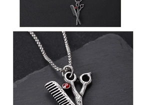 Close-up of vintage silver scissor and comb pendant with red rhinestones on black background