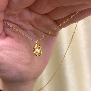 Close-up of golden irregular lava-shaped pendant necklace with a white pearl inlay