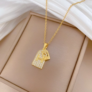 Close-up of golden titanium necklace with double H-letter pendants and zircon stones