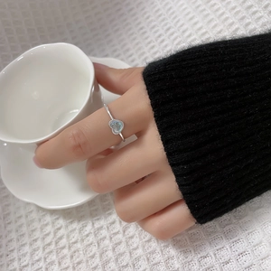 Close-up of heart-shaped moonstone ring on model's finger with a minimalist silver band