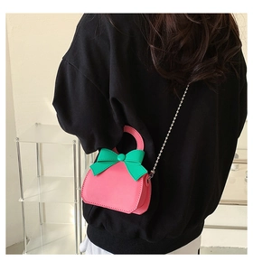 Detail view of pink mini crossbody bag with green bow and silver chain on model