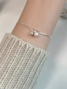 Detail view of double-layer silver bracelet with pearl and bead on a model's wrist
