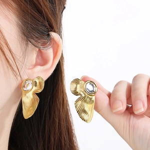 Detailed macro view of gold square earrings with irregular metal folds and center zircon