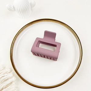 Detail of matte dark purple rectangular hair claw clip displayed on an elegant white plate