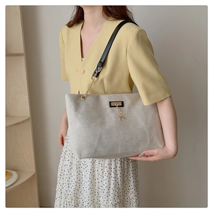 Close-up of cream canvas tote bag with black leather strap and gold deer charm detail