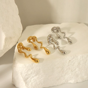 Détail de boucles d'oreilles fluides ondulées en or et argent sur une pierre blanche